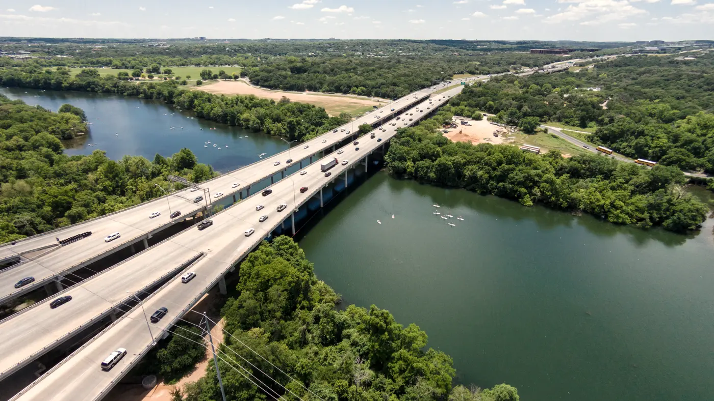 Aerial view of a highway bridge crossing a green Austin river valley