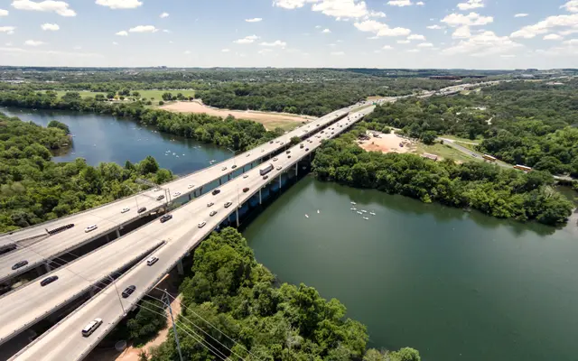 Aerial view of a highway bridge crossing a green Austin river valley