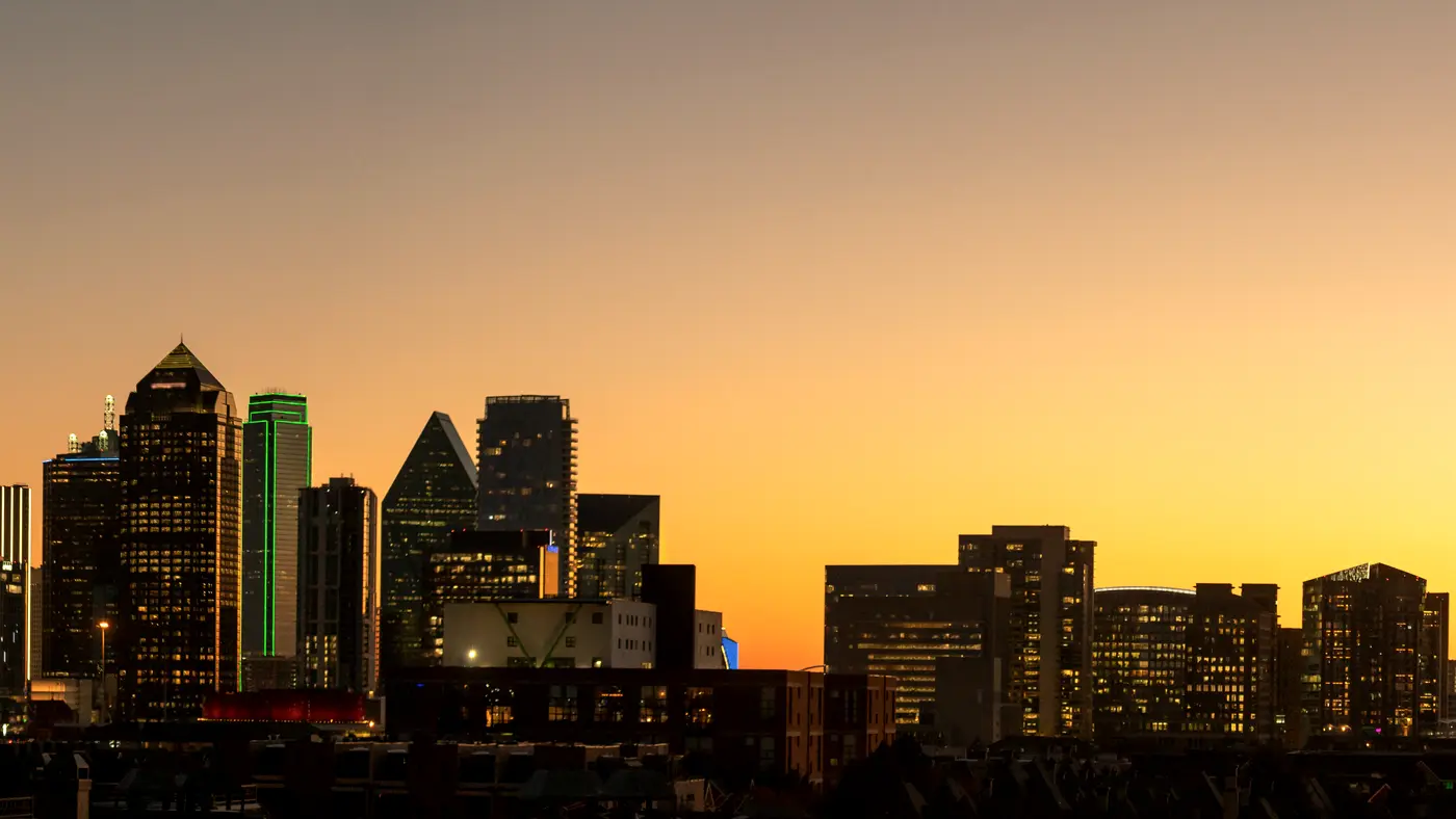 Dallas skyline silhouetted against an orange sunset sky