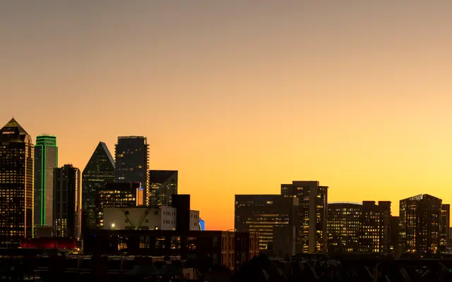 Dallas skyline silhouetted against an orange sunset sky