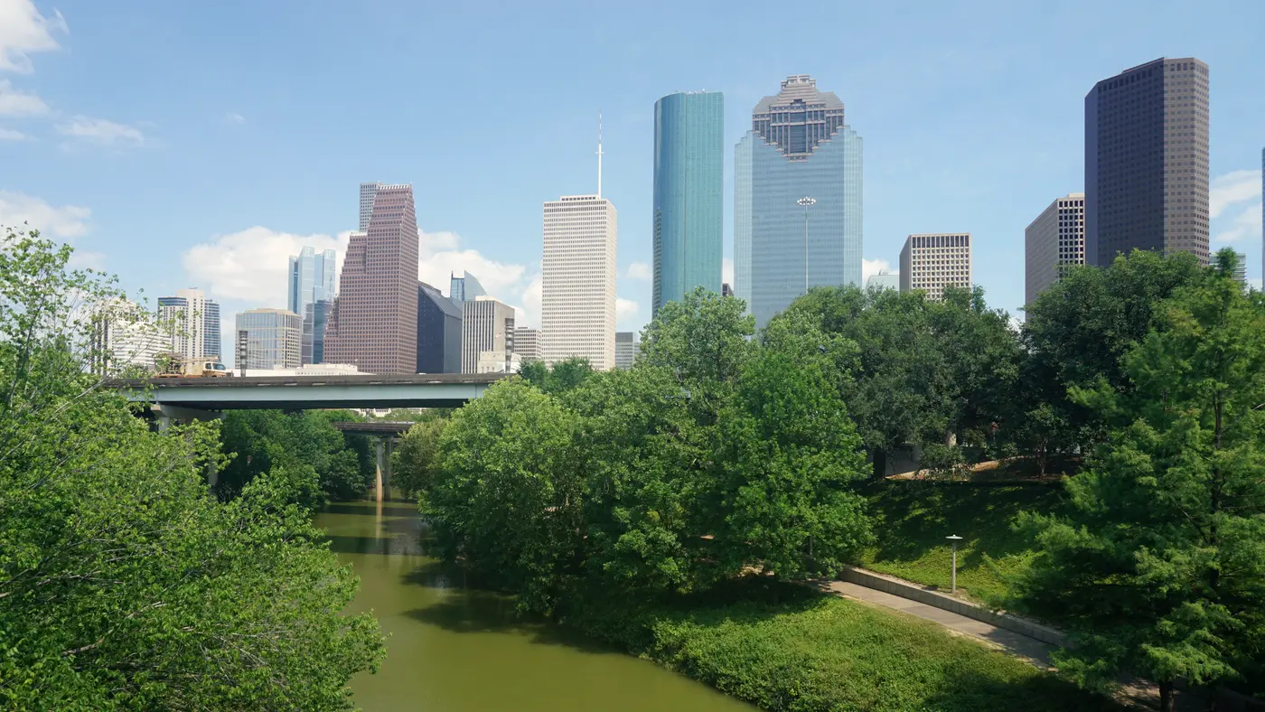 Houston skyscrapers over leafy trees along Buffalo Bayou on a bright day