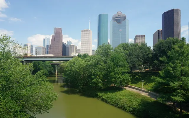 Houston skyscrapers over leafy trees along Buffalo Bayou on a bright day