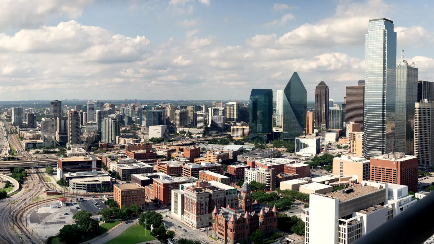 Aerial view of downtown Dallas skyline under scattered clouds
