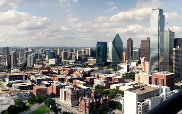 Aerial view of downtown Dallas skyline under scattered clouds