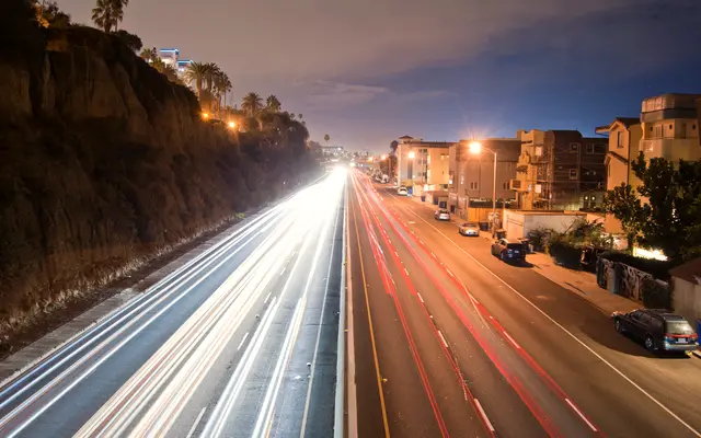 Evening traffic light trails on a highway beside a cliff