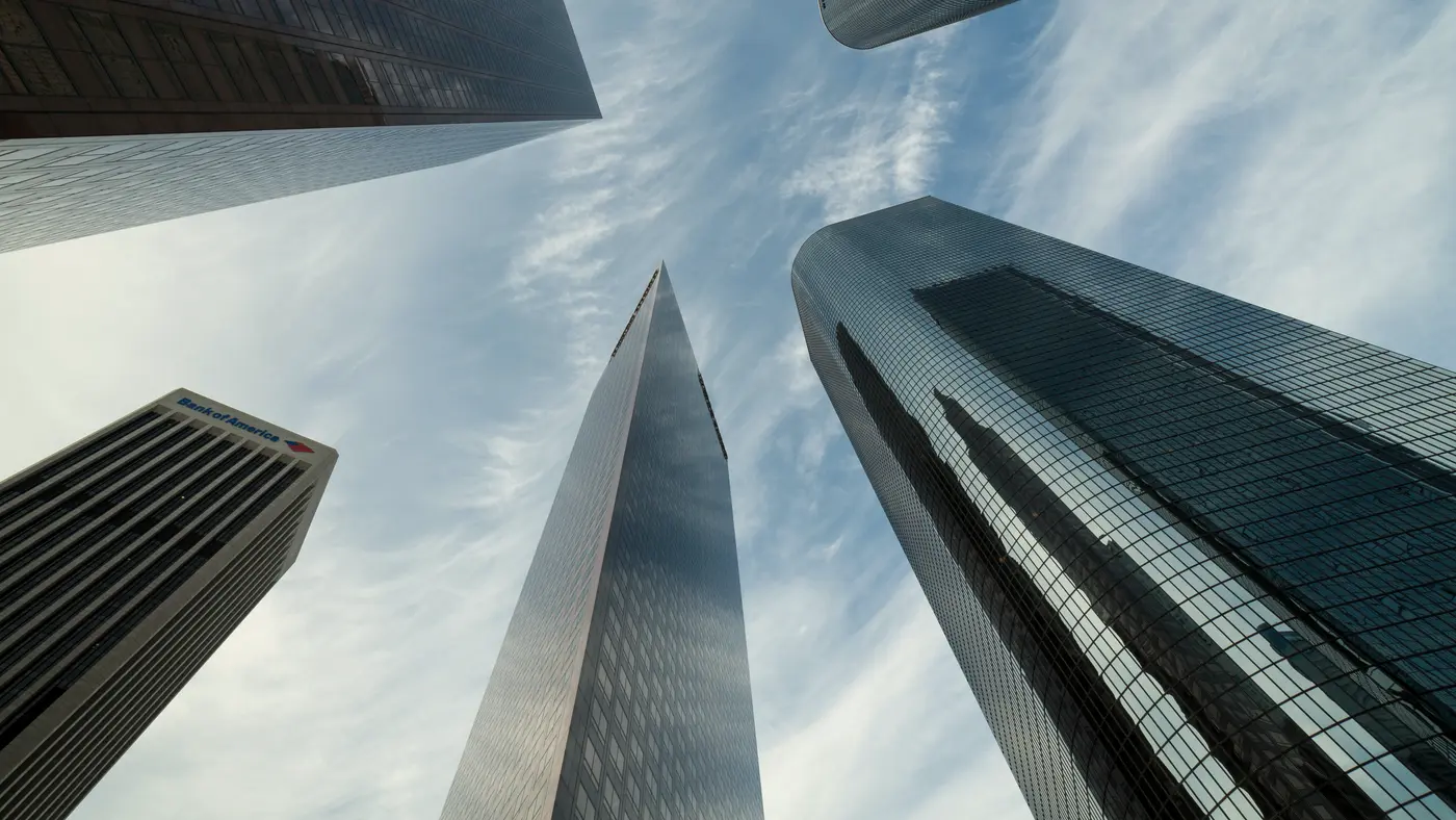 Looking up at glass skyscrapers converging against a cloudy sky