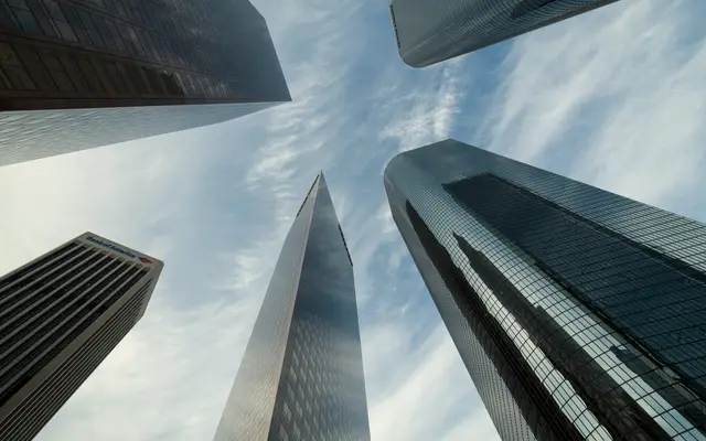 Looking up at glass skyscrapers converging against a cloudy sky