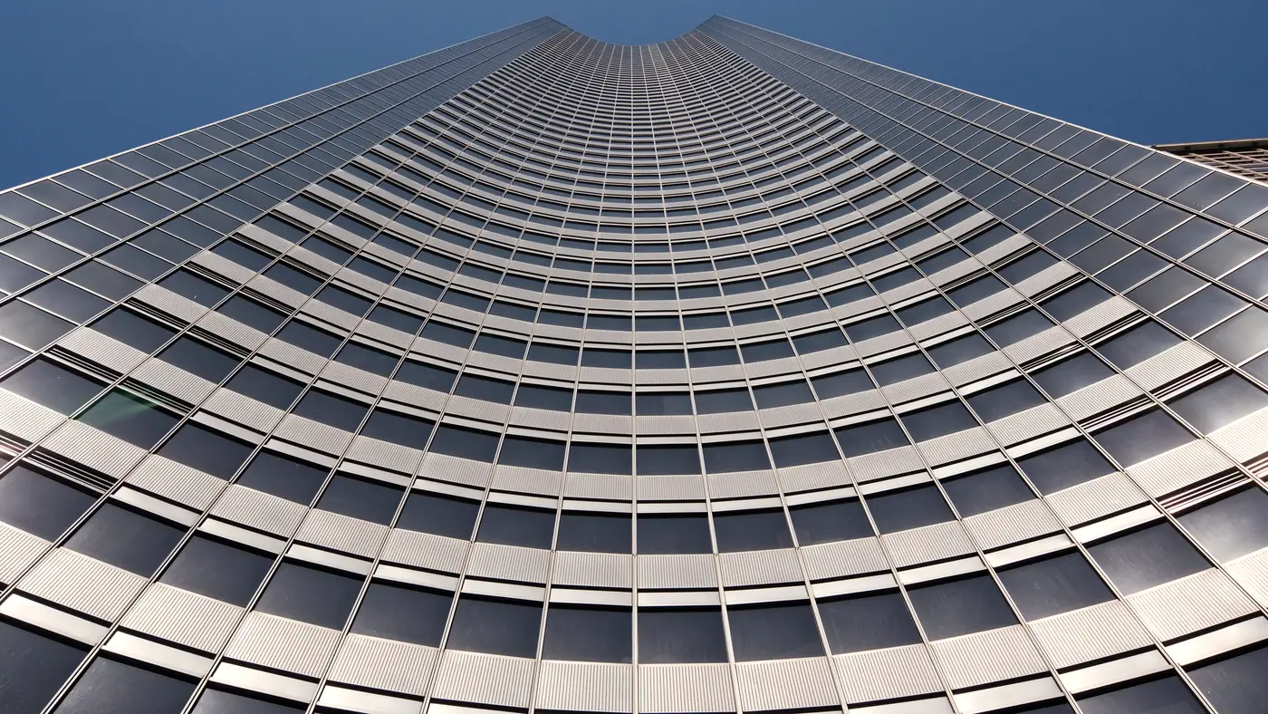 Curved glass office tower seen from below against deep blue sky