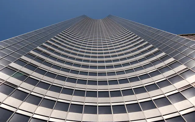 Curved glass office tower seen from below against deep blue sky
