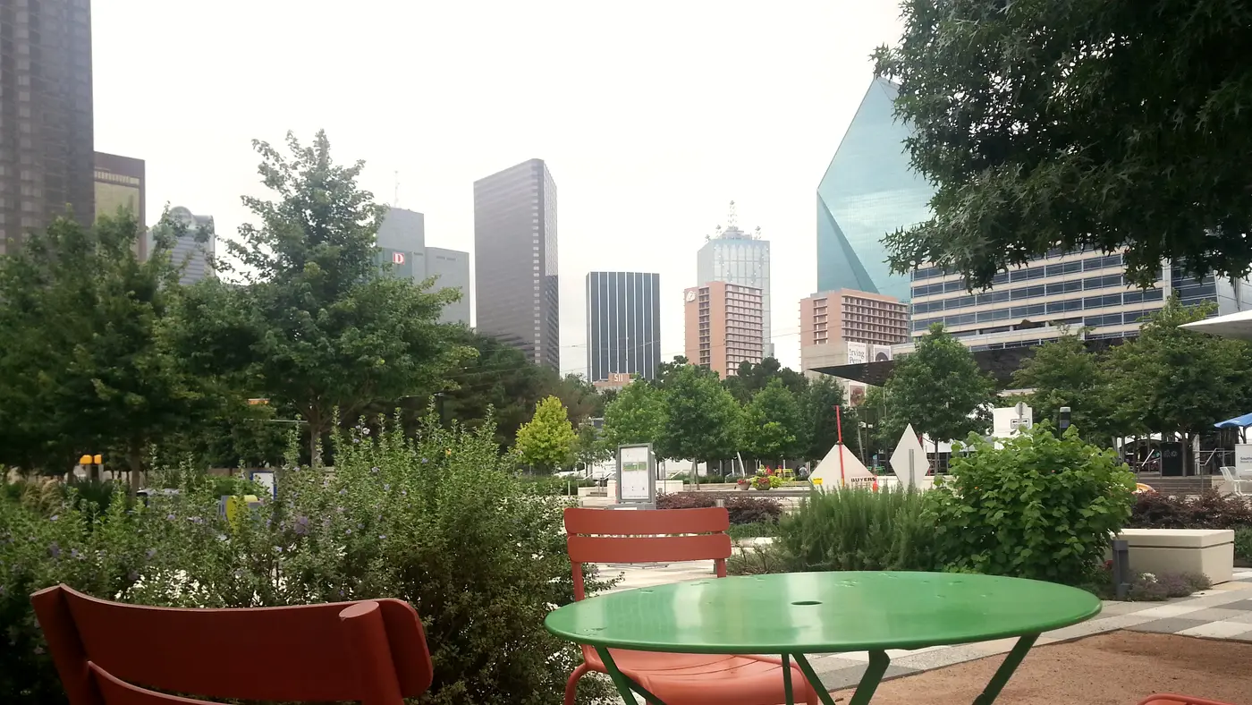 Green cafe table in a Dallas park below skyline towers