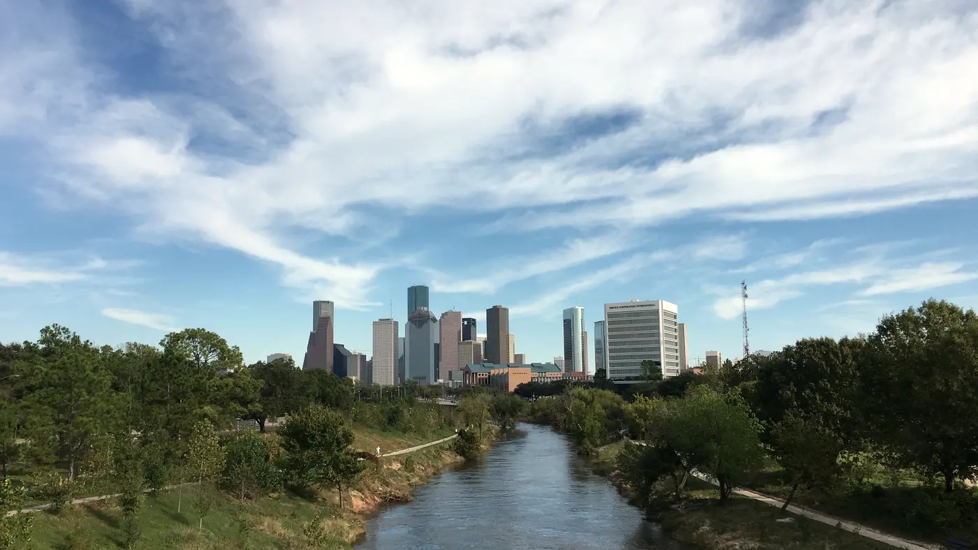 Buffalo Bayou winding toward the distant Houston skyline under wispy clouds