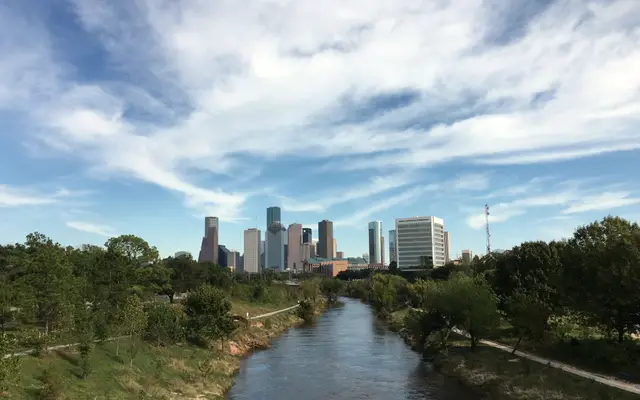Buffalo Bayou winding toward the distant Houston skyline under wispy clouds