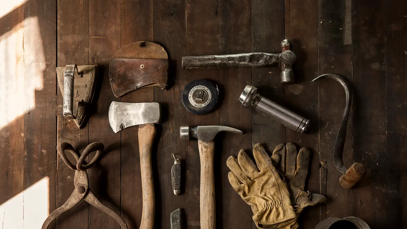 Hammer, axe, pliers and work gloves laid out on wood