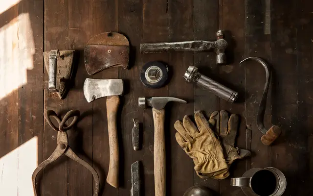 Hammer, axe, pliers and work gloves laid out on wood