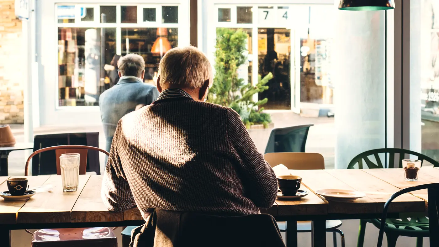 Older man sitting at a table inside a bright cafe