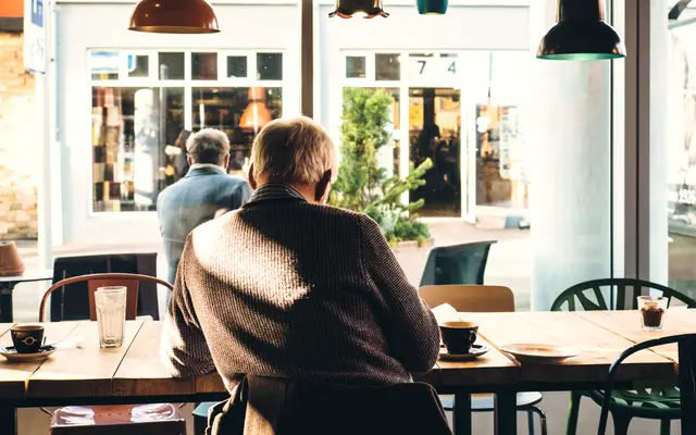 Older man sitting at a table inside a bright cafe