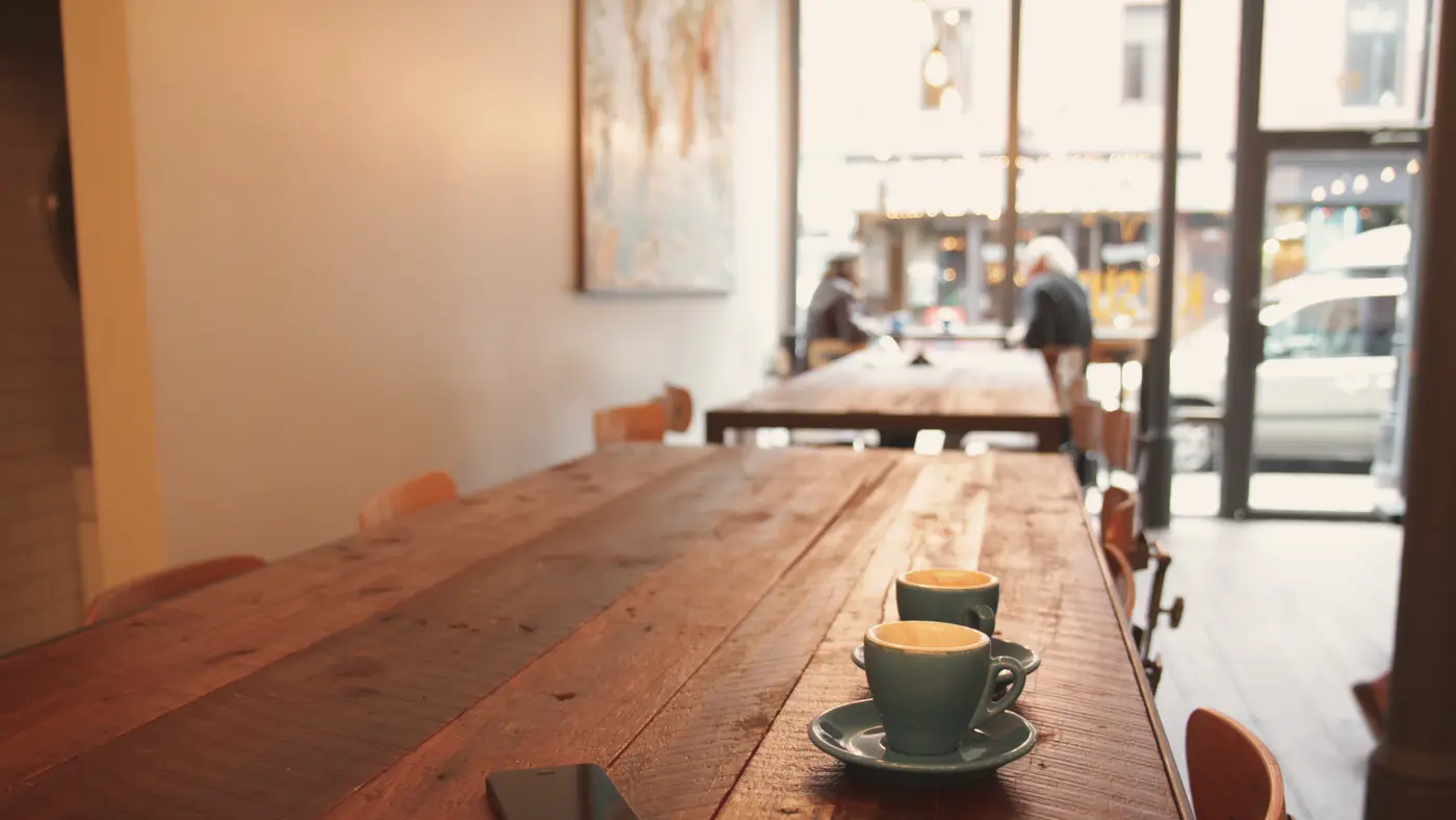 Long wooden table with coffee cups in a small cafe