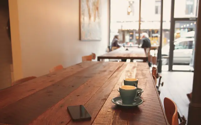 Long wooden table with coffee cups in a small cafe