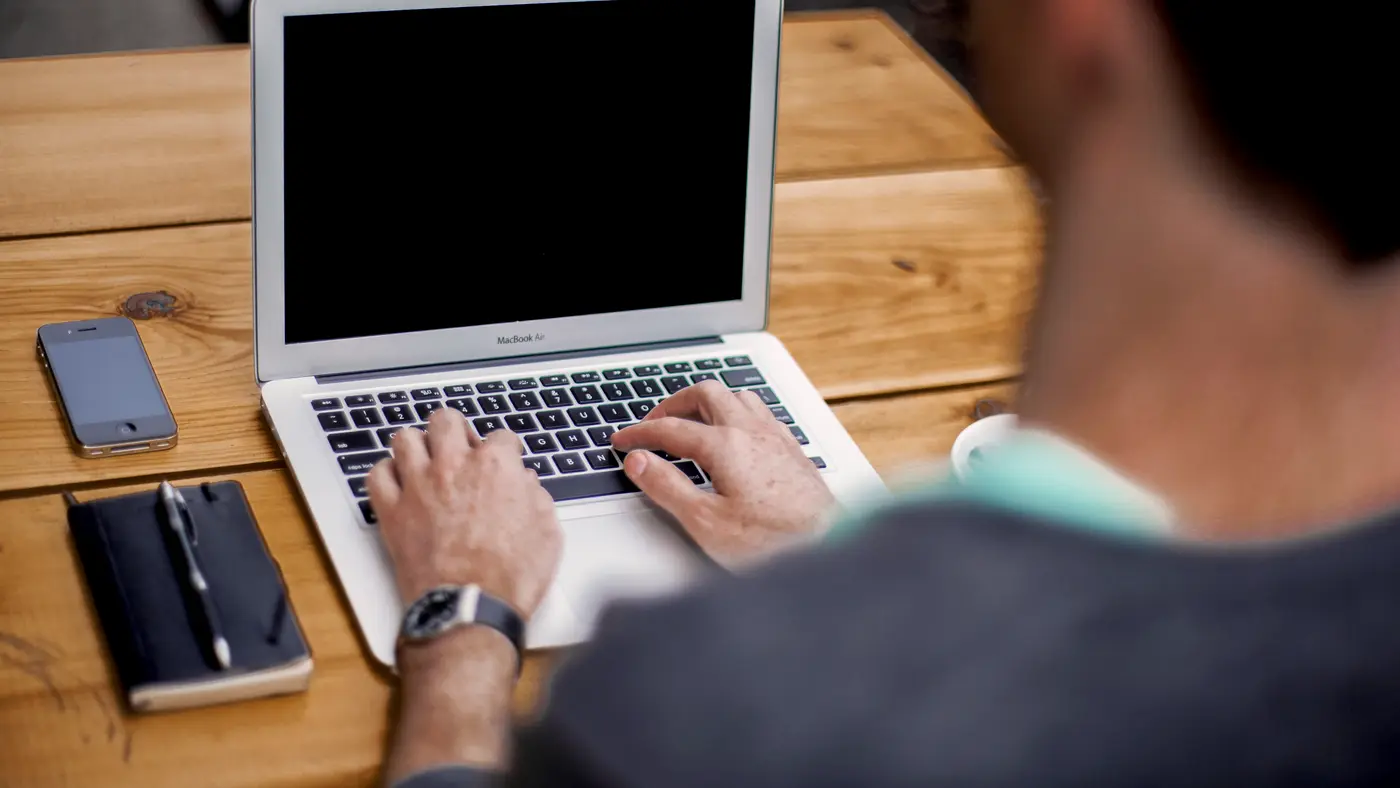 Man typing on a laptop at a wooden desk
