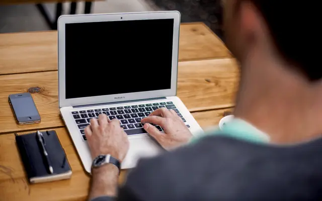 Man typing on a laptop at a wooden desk