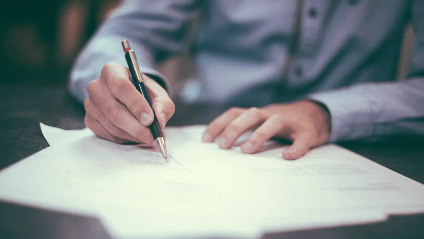 Man in a shirt signing a document at a desk