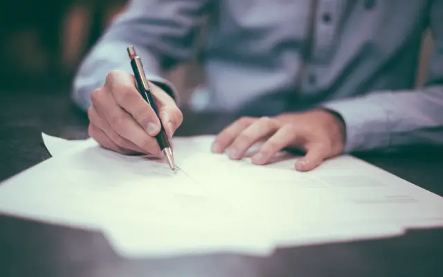 Man in a shirt signing a document at a desk