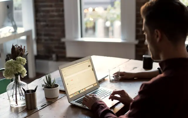 Man working on a laptop at a desk by a window