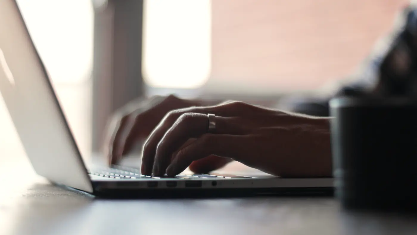 Hands typing on a laptop at a bright desk