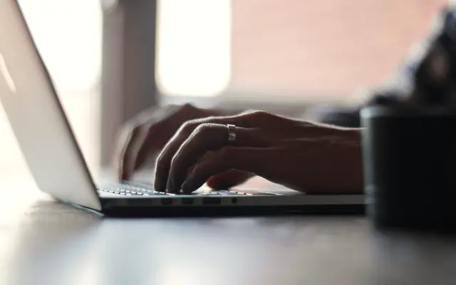 Hands typing on a laptop at a bright desk