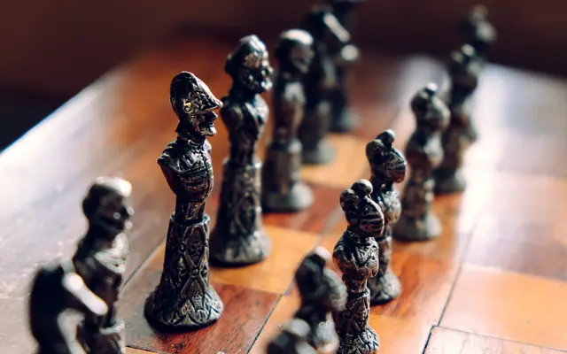 Ornate metal chess pieces lined up on a wooden board