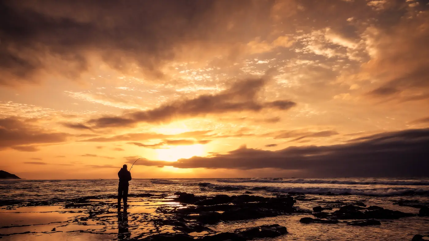 Lone figure on a rocky shoreline under a golden sunset