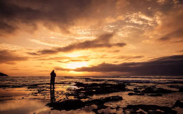 Lone figure on a rocky shoreline under a golden sunset