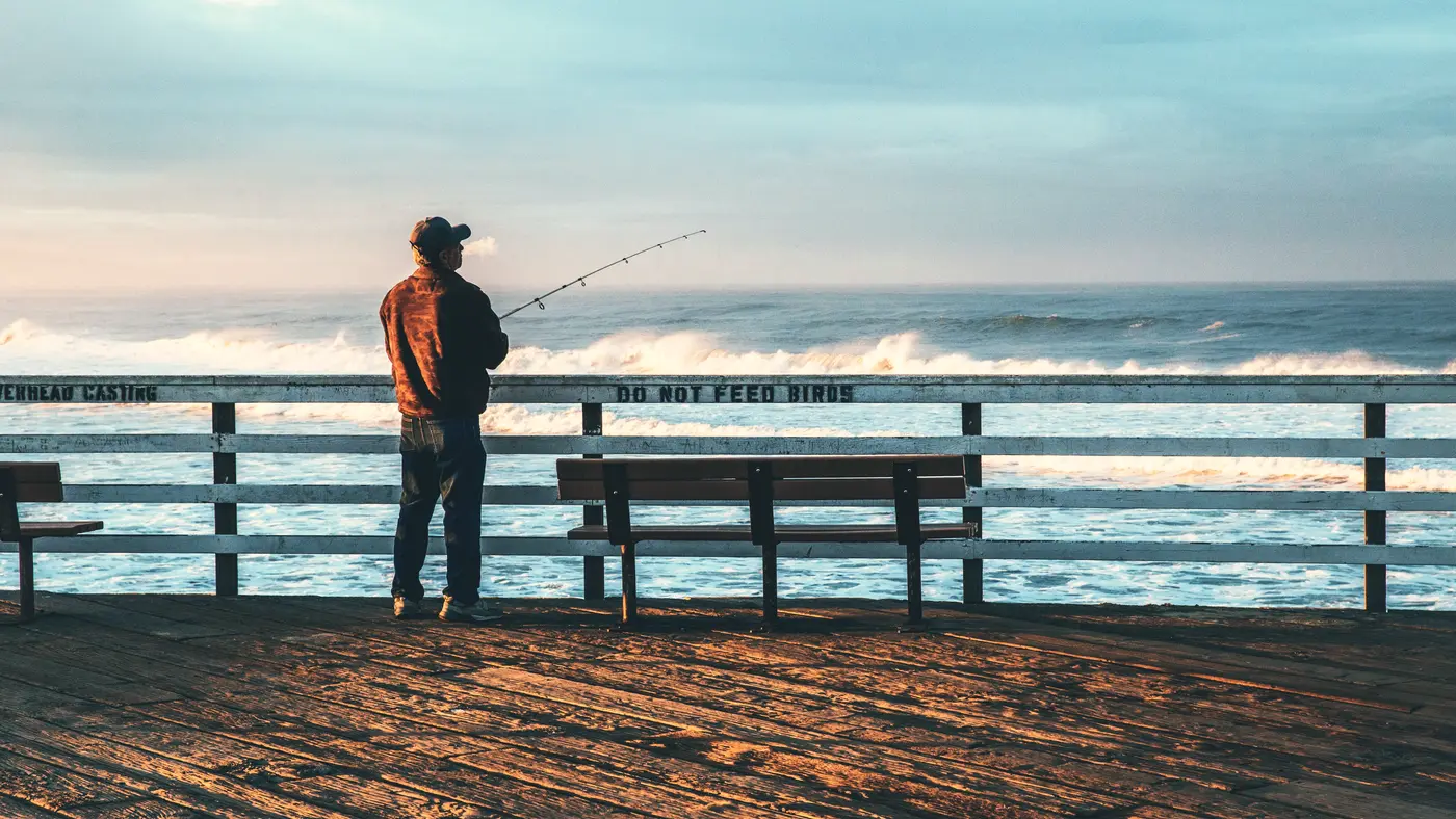 Man fishing from a wooden pier on a bright morning