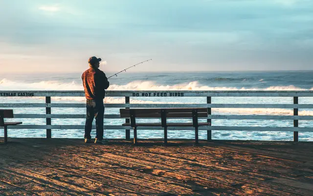 Man fishing from a wooden pier on a bright morning