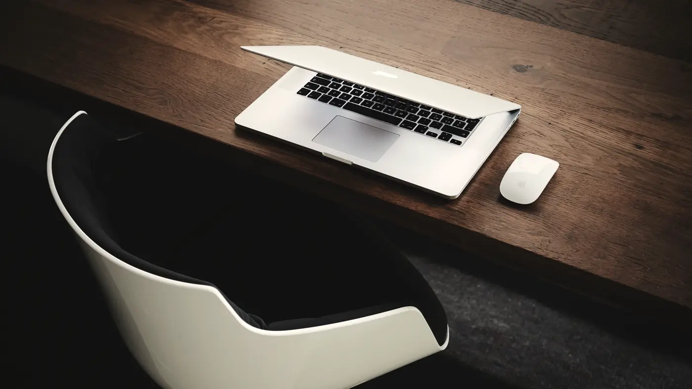 Laptop on a dark wooden desk with a white chair
