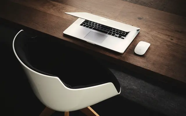 Laptop on a dark wooden desk with a white chair