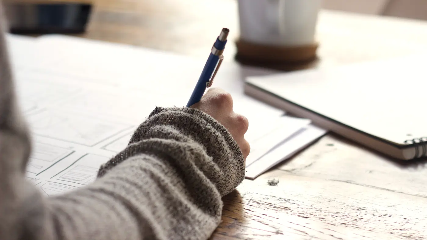 Person writing notes on paper beside a coffee mug