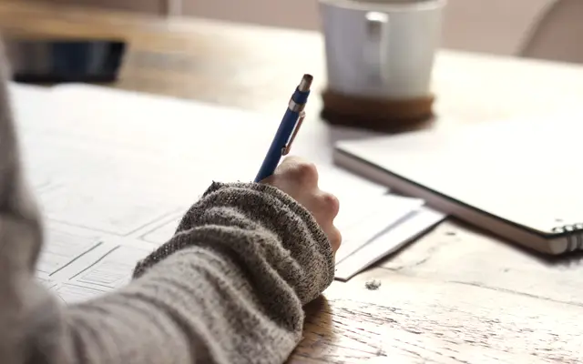 Person writing notes on paper beside a coffee mug