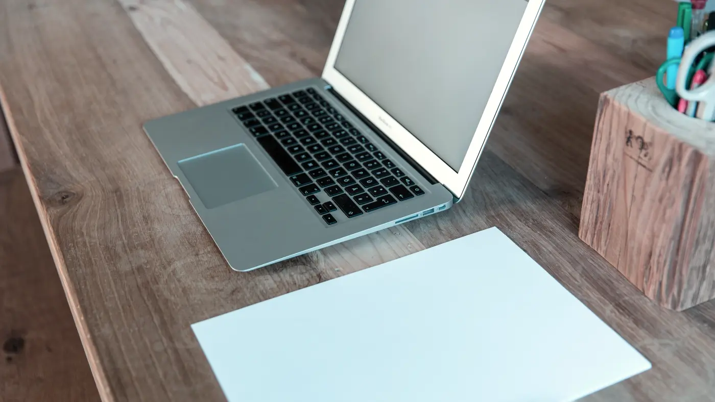Open laptop and blank sheet of paper on a wooden desk