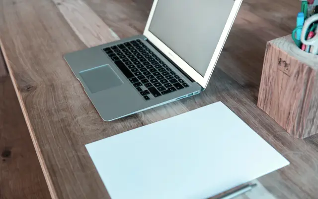 Open laptop and blank sheet of paper on a wooden desk