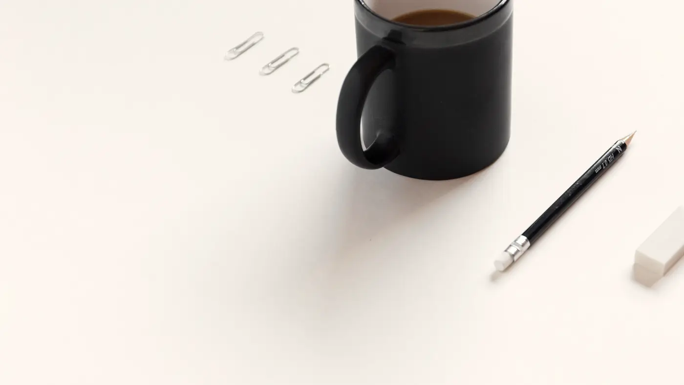 Black coffee mug, pencil and paper clips on a white desk