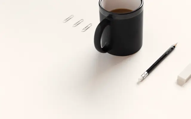Black coffee mug, pencil and paper clips on a white desk
