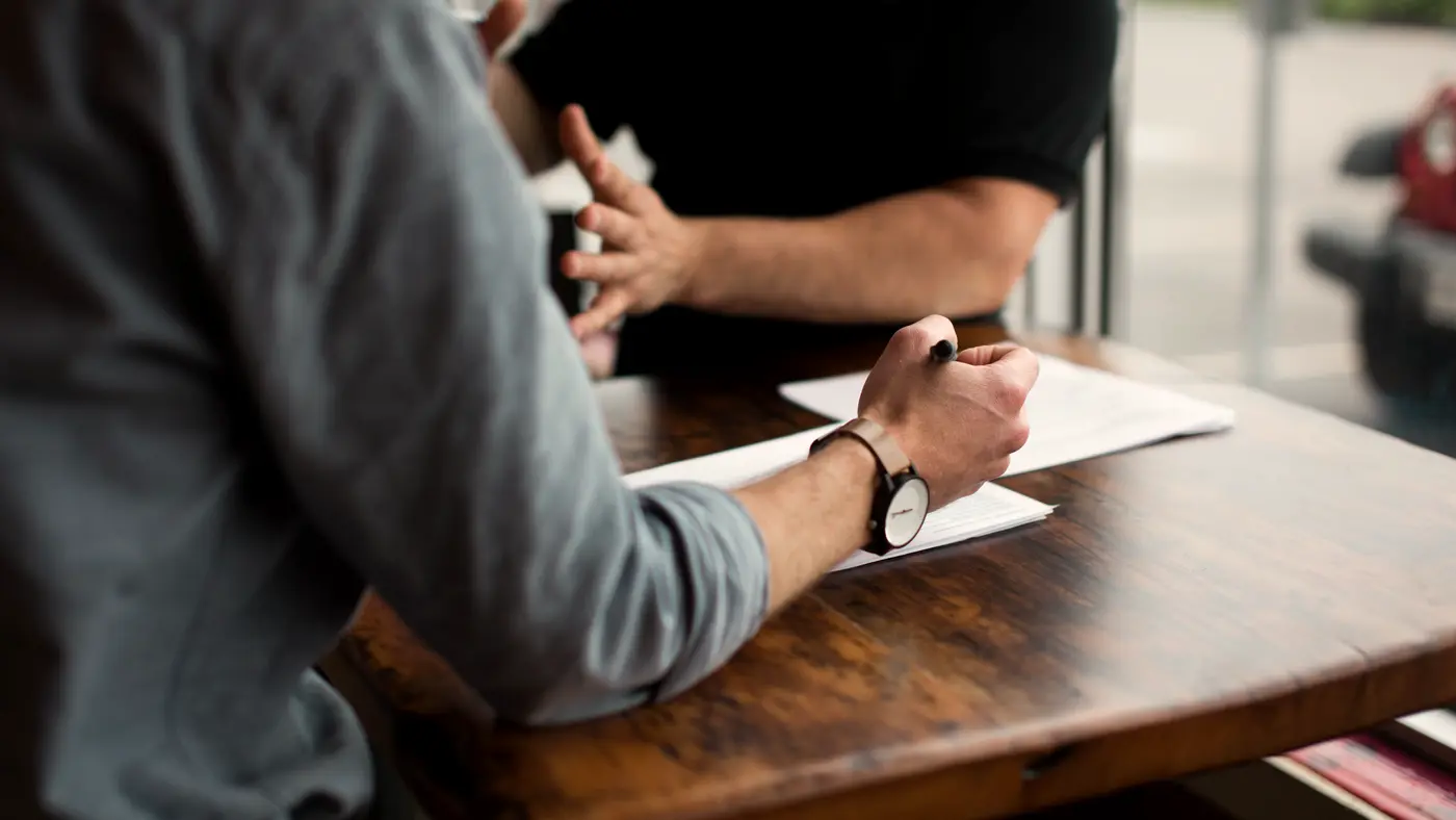 Two people signing papers across a wooden table