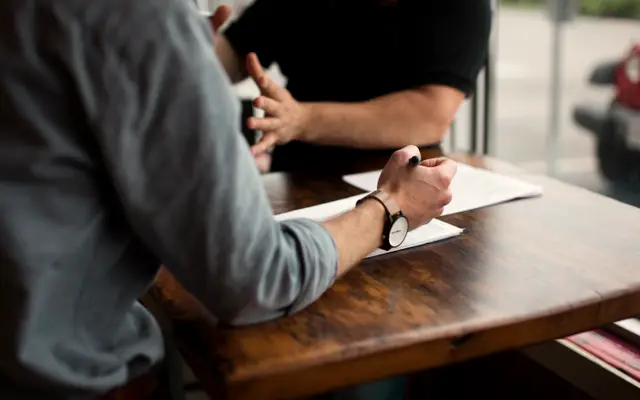 Two people signing papers across a wooden table