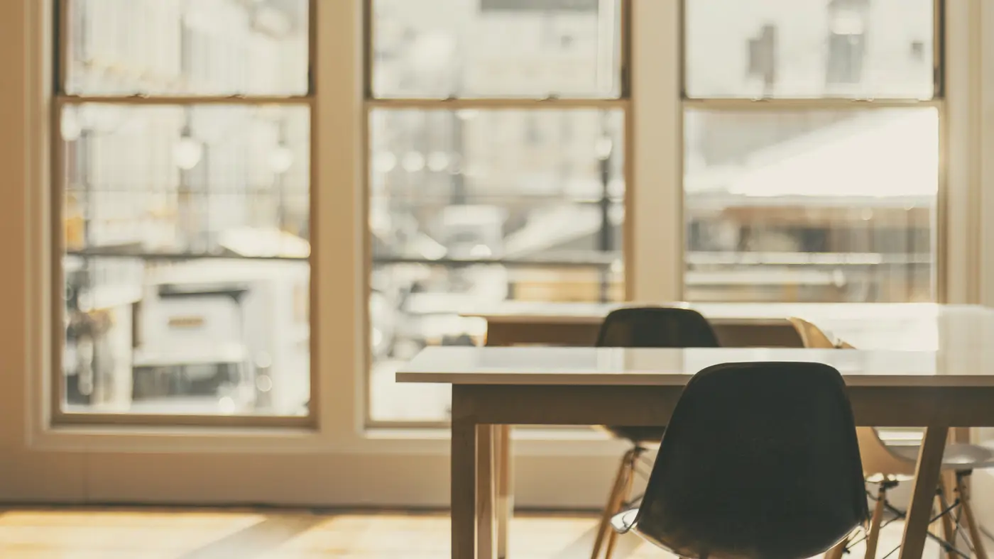 Empty meeting table and chairs beside tall bright windows