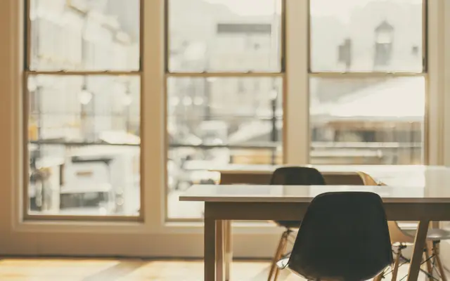 Empty meeting table and chairs beside tall bright windows