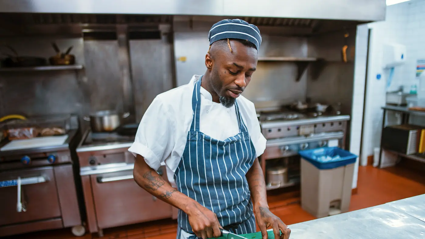 Chef in striped apron chopping vegetables in a commercial kitchen