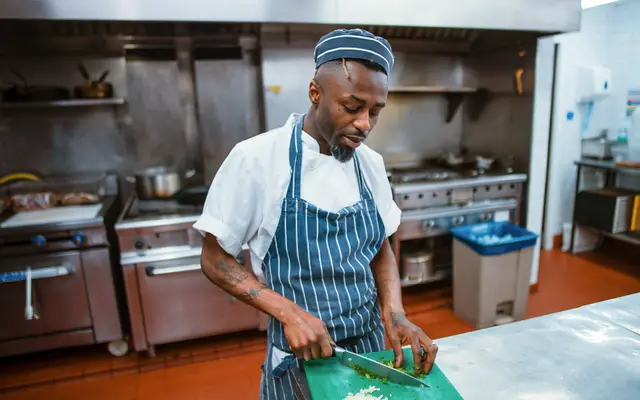 Chef in striped apron chopping vegetables in a commercial kitchen