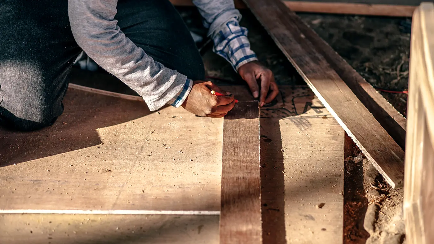 Carpenter kneeling to mark wooden boards on a work floor