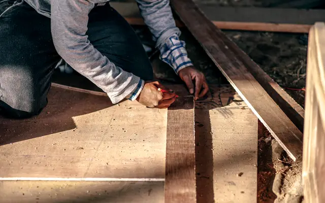 Carpenter kneeling to mark wooden boards on a work floor